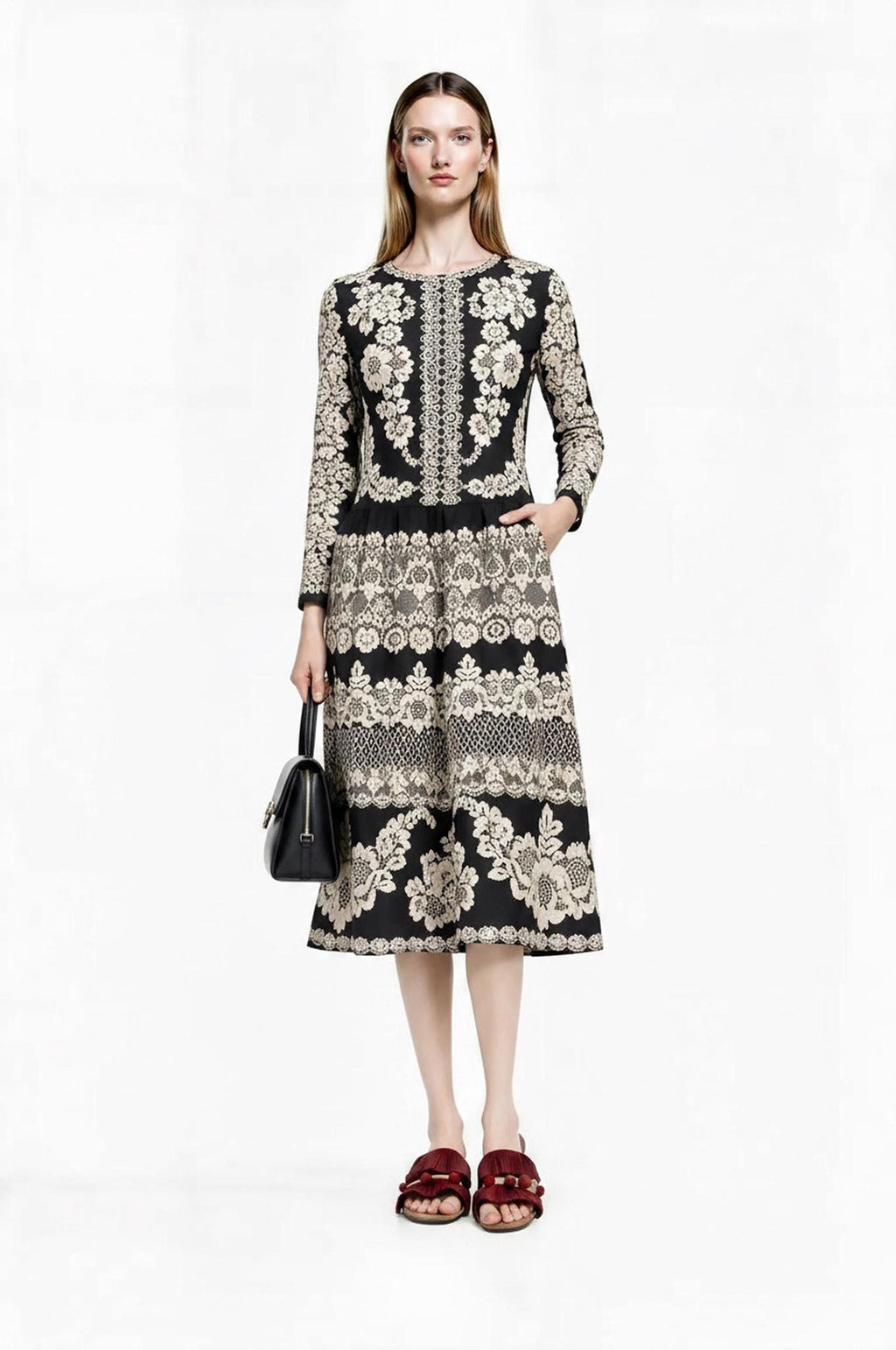 Front view of the model wearing the black and ivory floral dress while holding a small black handbag.