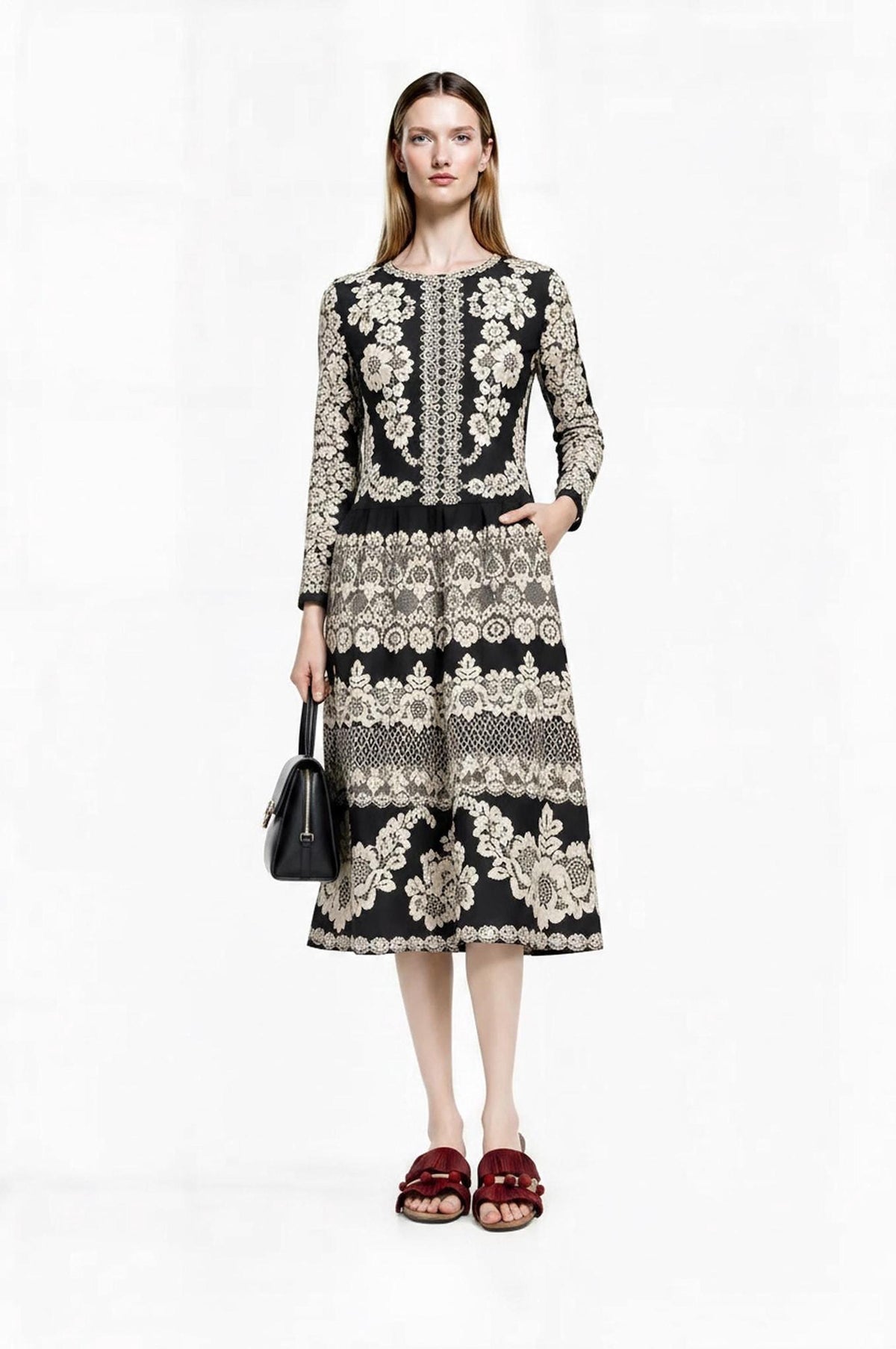 Front view of the model wearing the black and ivory floral dress while holding a small black handbag.