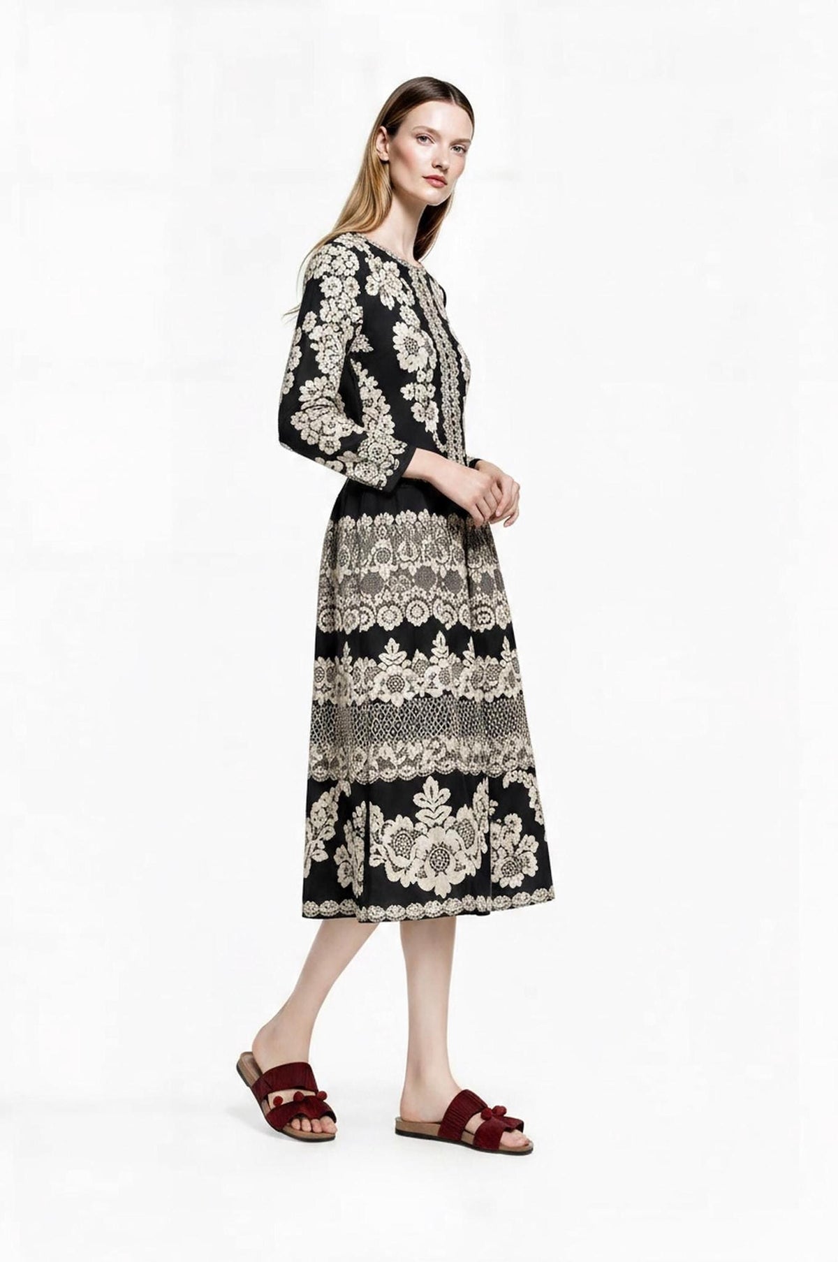 Three-quarter side view of the model posing in the long-sleeved black and ivory patterned midi dress.