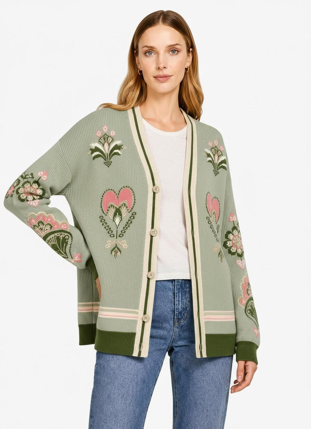 A woman modeling a sage green knit cardigan with pink and white folk-style floral patterns on the front and sleeves.