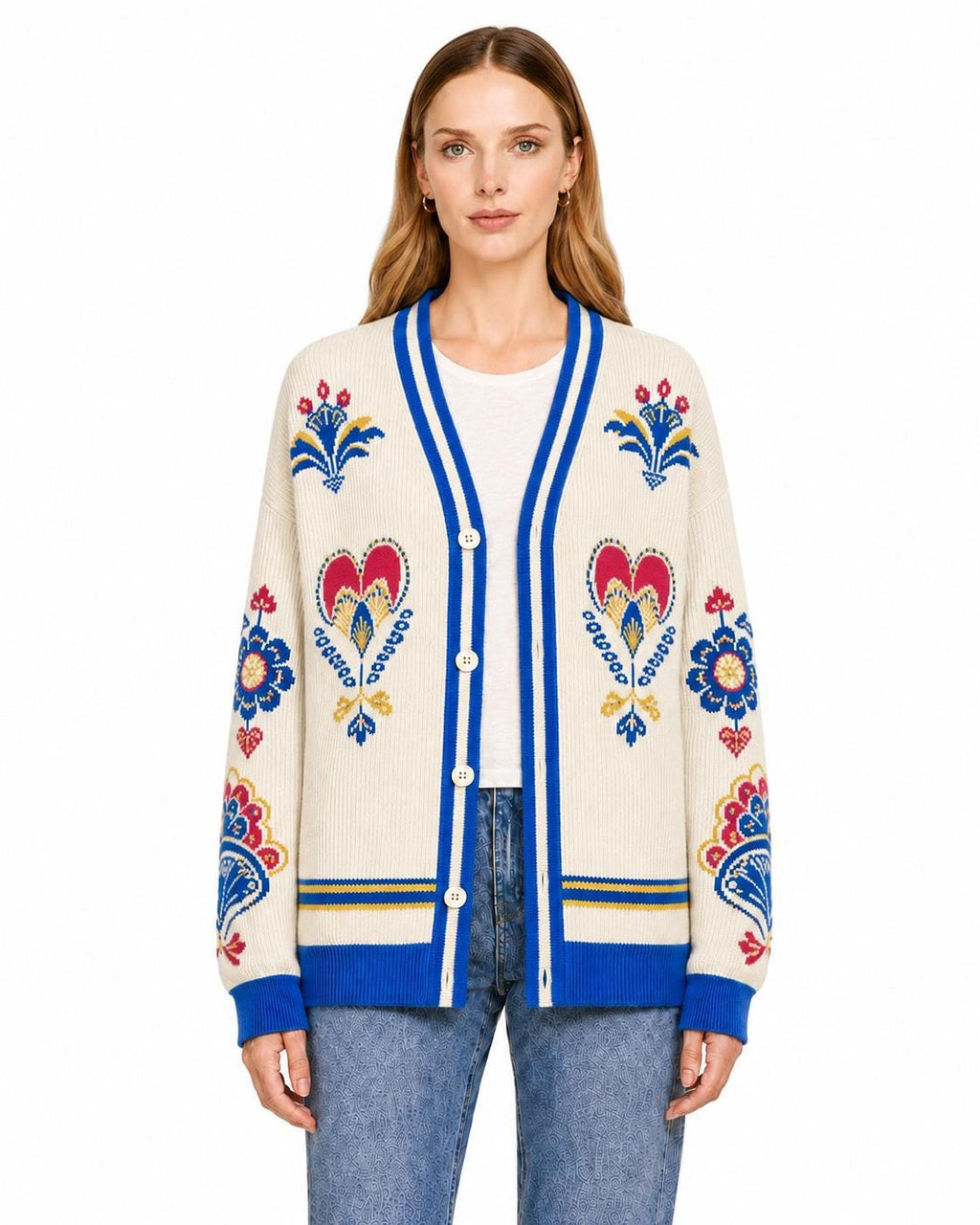 A model wearing an ivory knit cardigan with bright blue trim and colorful folk-inspired floral and heart patterns.