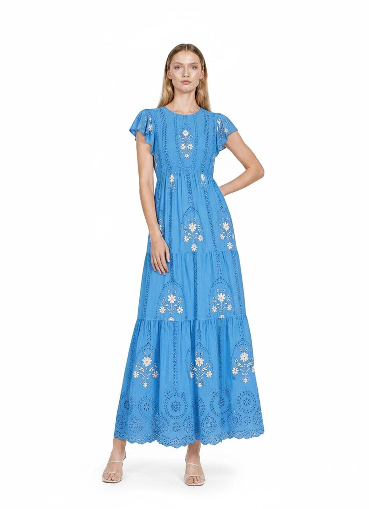 A model standing squarely to the front in a bright blue tiered maxi dress with white floral embroidery and short flutter sleeves.
