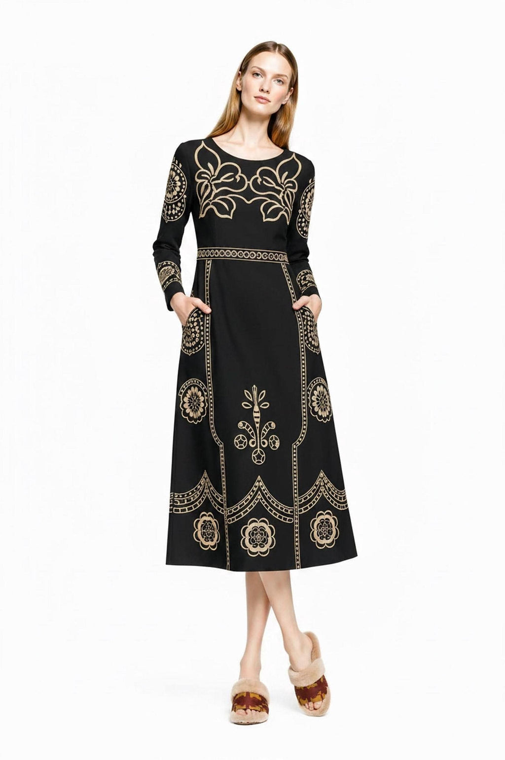 A model stands facing forward with hands in the pockets of the black and beige folk print midi dress.