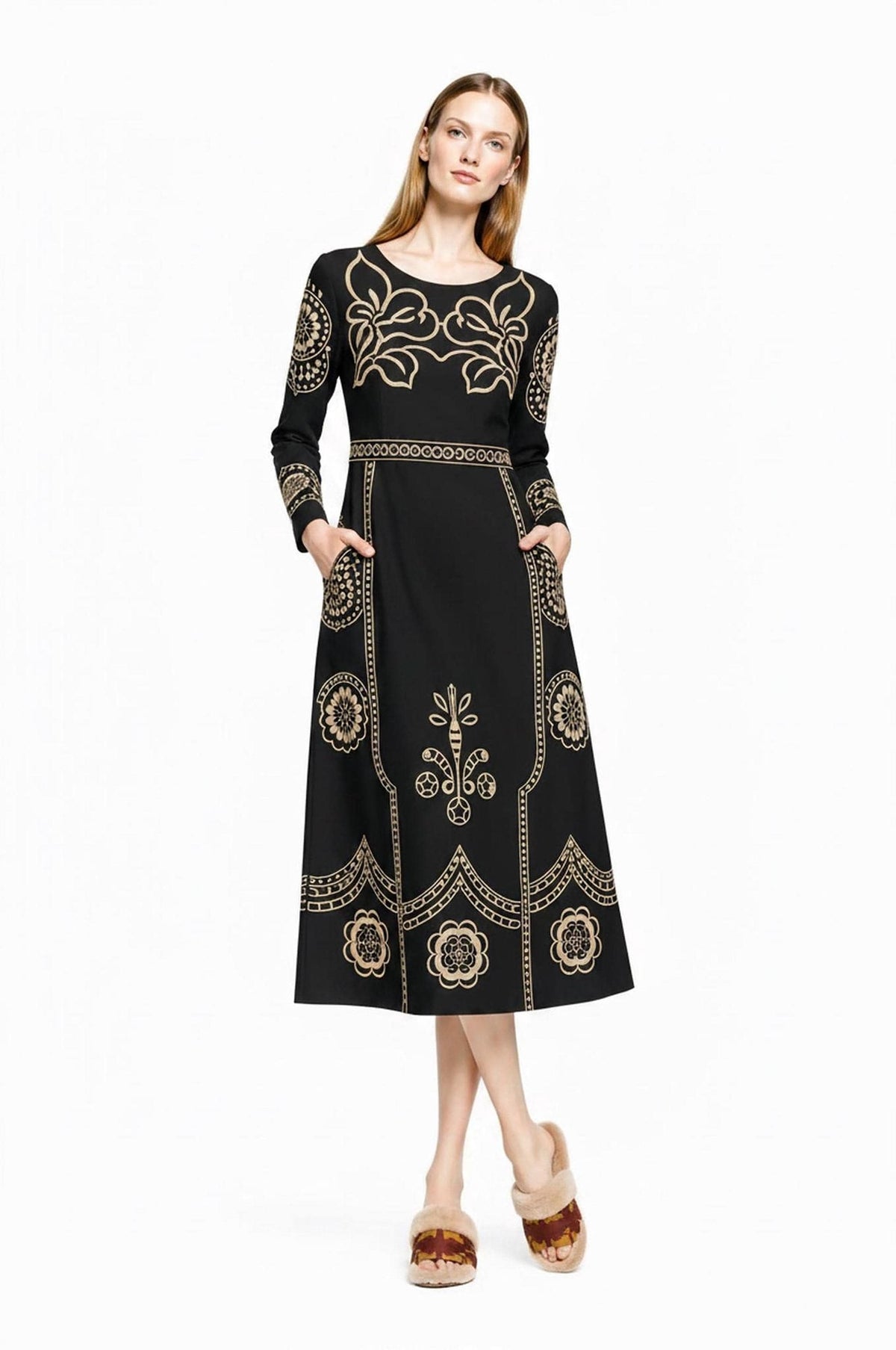 A model stands facing forward with hands in the pockets of the black and beige folk print midi dress.