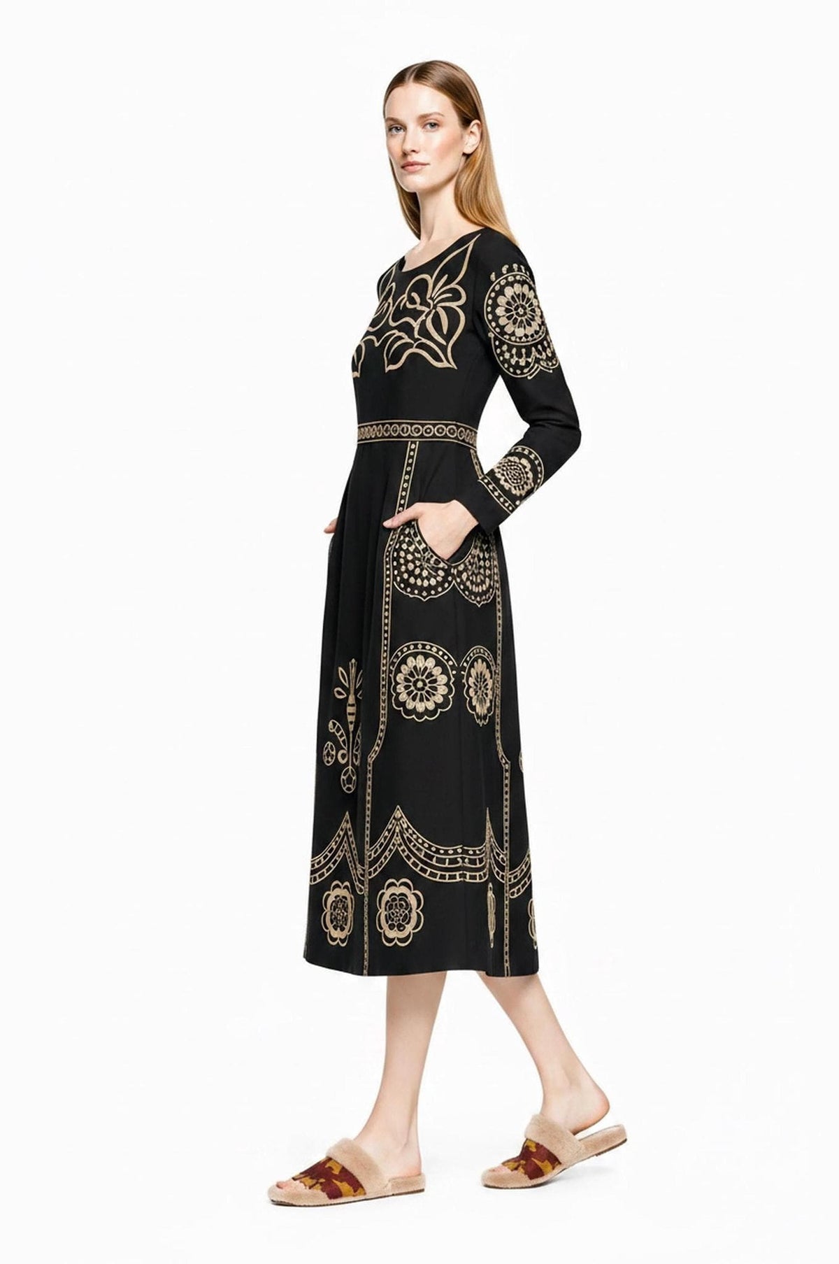 A profile view of a model wearing the black long-sleeve midi dress featuring intricate beige folk designs along the skirt and bodice.