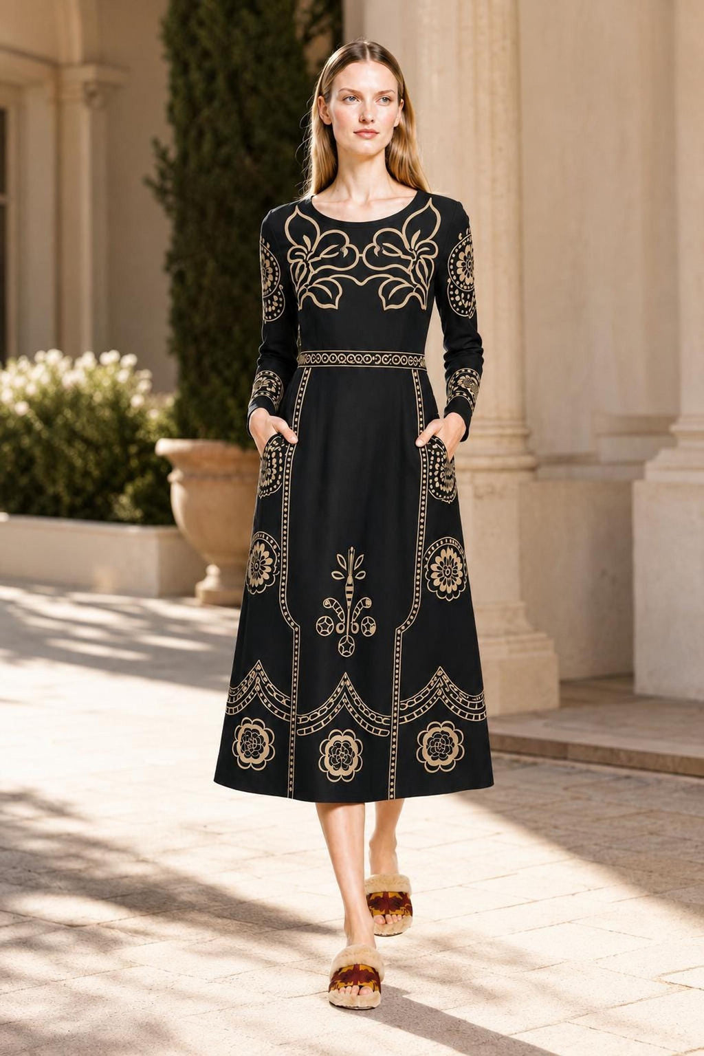 A model walks outdoors on a sunny day along a stone pathway wearing the long-sleeve black midi dress.