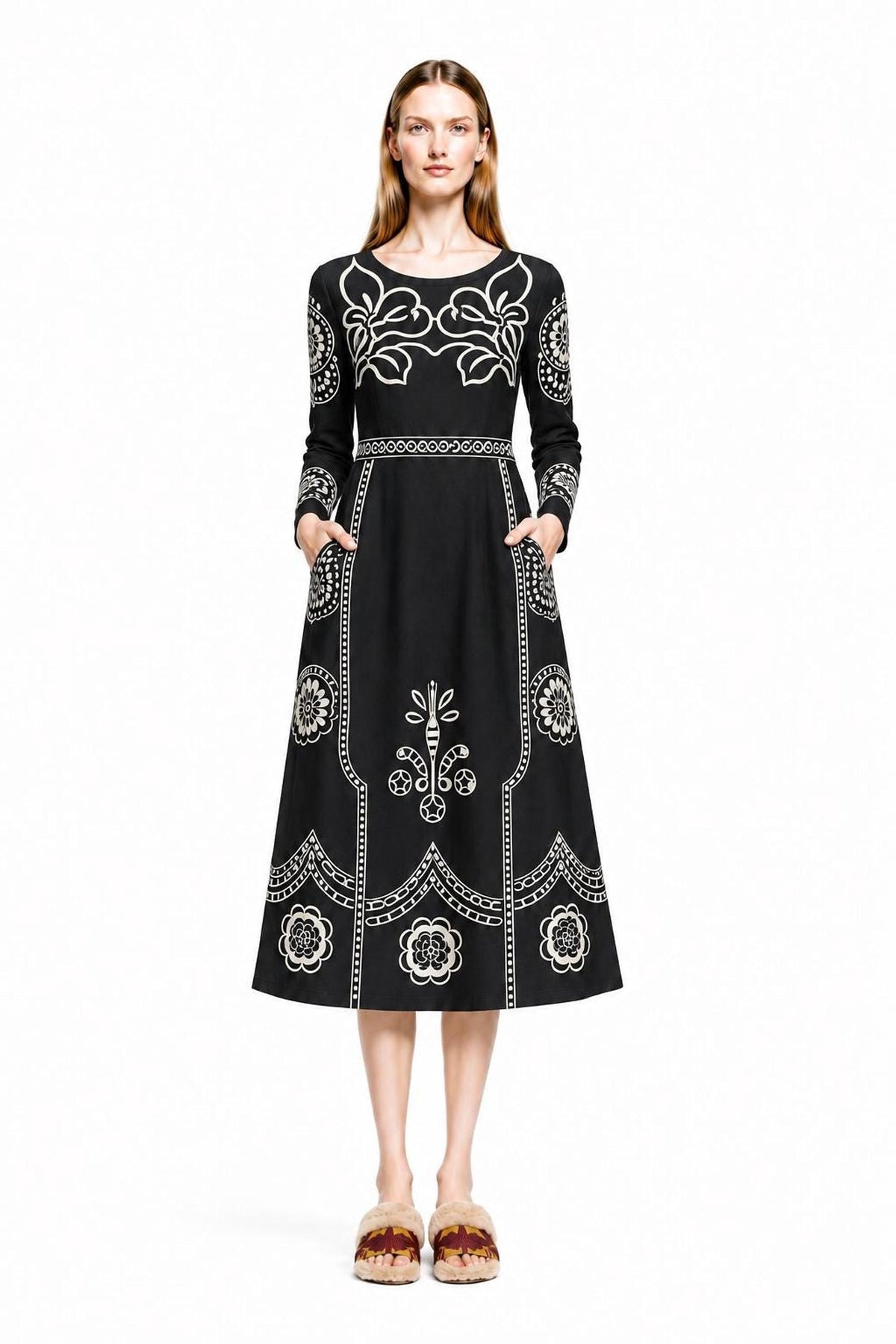 A model stands facing forward wearing a black midi dress with white folk floral print against a plain white background.