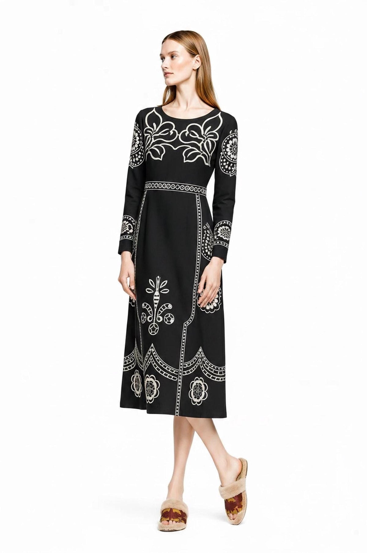 A model stands angled against a white background, wearing a black long-sleeve midi dress featuring a beige folk floral print and pockets.