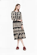 May include: A long-sleeved midi dress featuring a black base with a repeating cream-colored floral and lace-inspired pattern. The garment has a round neckline, a fitted bodice, and a gathered skirt that falls below the knees, paired with dark red slides.