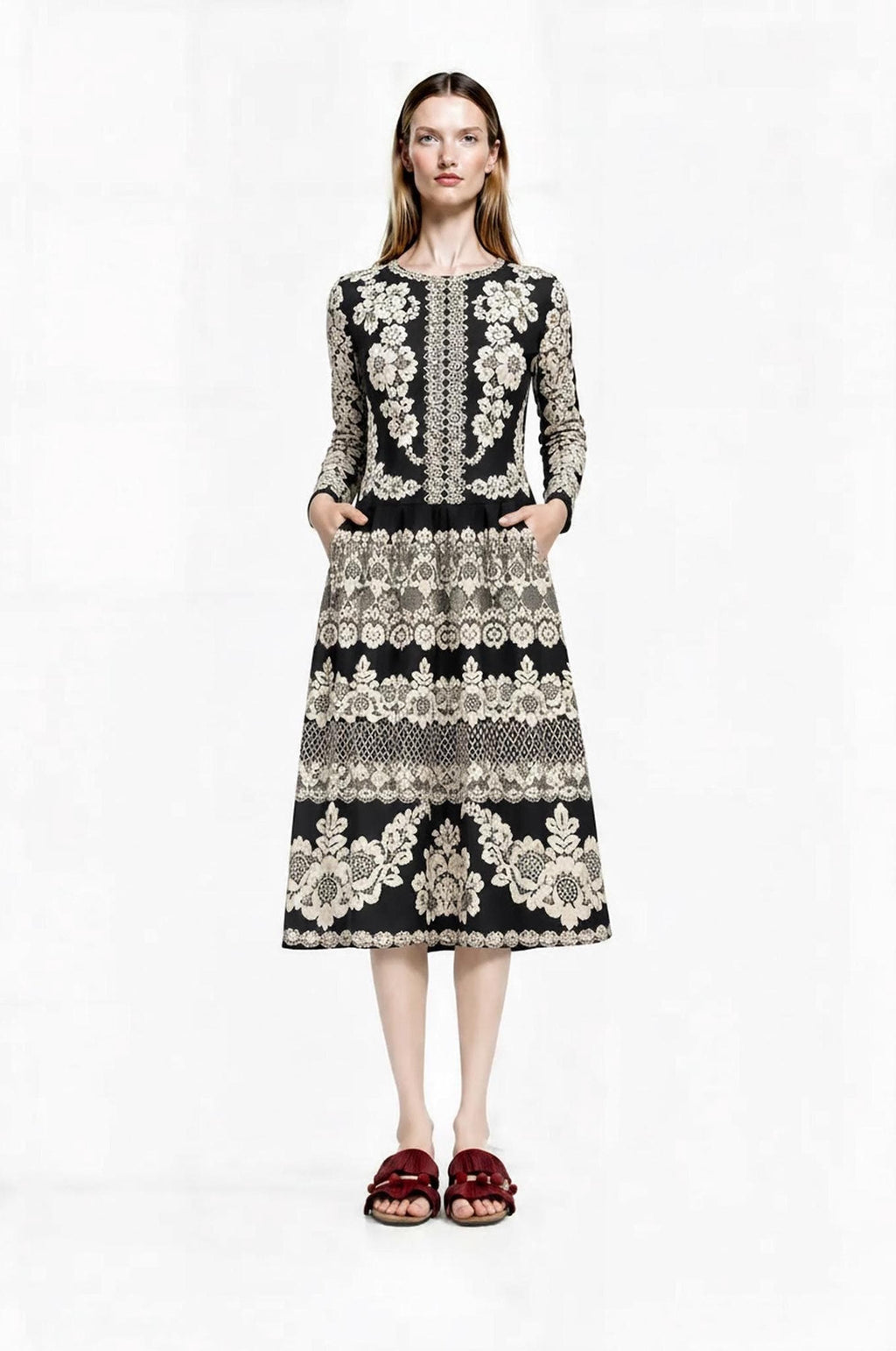 Front view of a model wearing a long-sleeved black midi dress with an ivory lace-look floral print and side pockets.