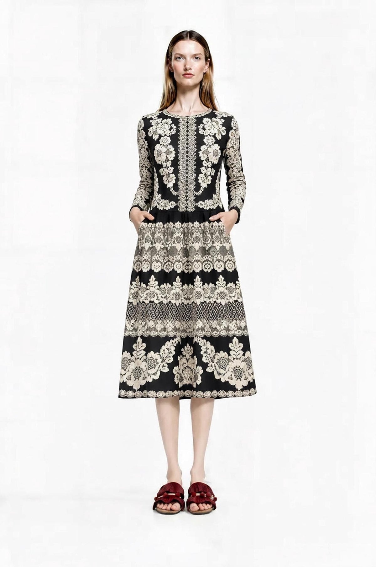 Front view of a model wearing a long-sleeved black midi dress with an ivory lace-look floral print and side pockets.