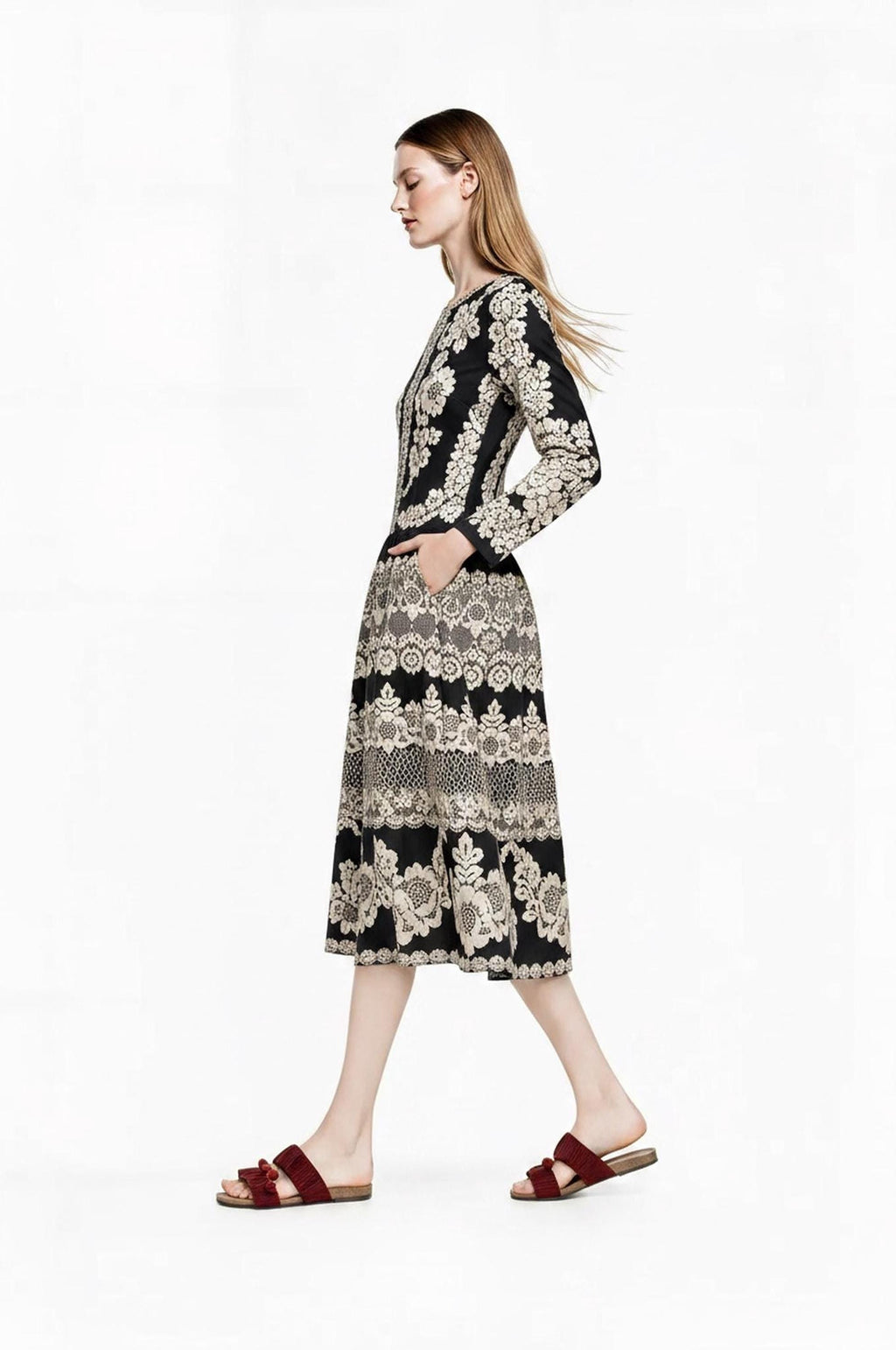 Profile view of the model walking forward with hair blowing, wearing the long-sleeve black and ivory dress.