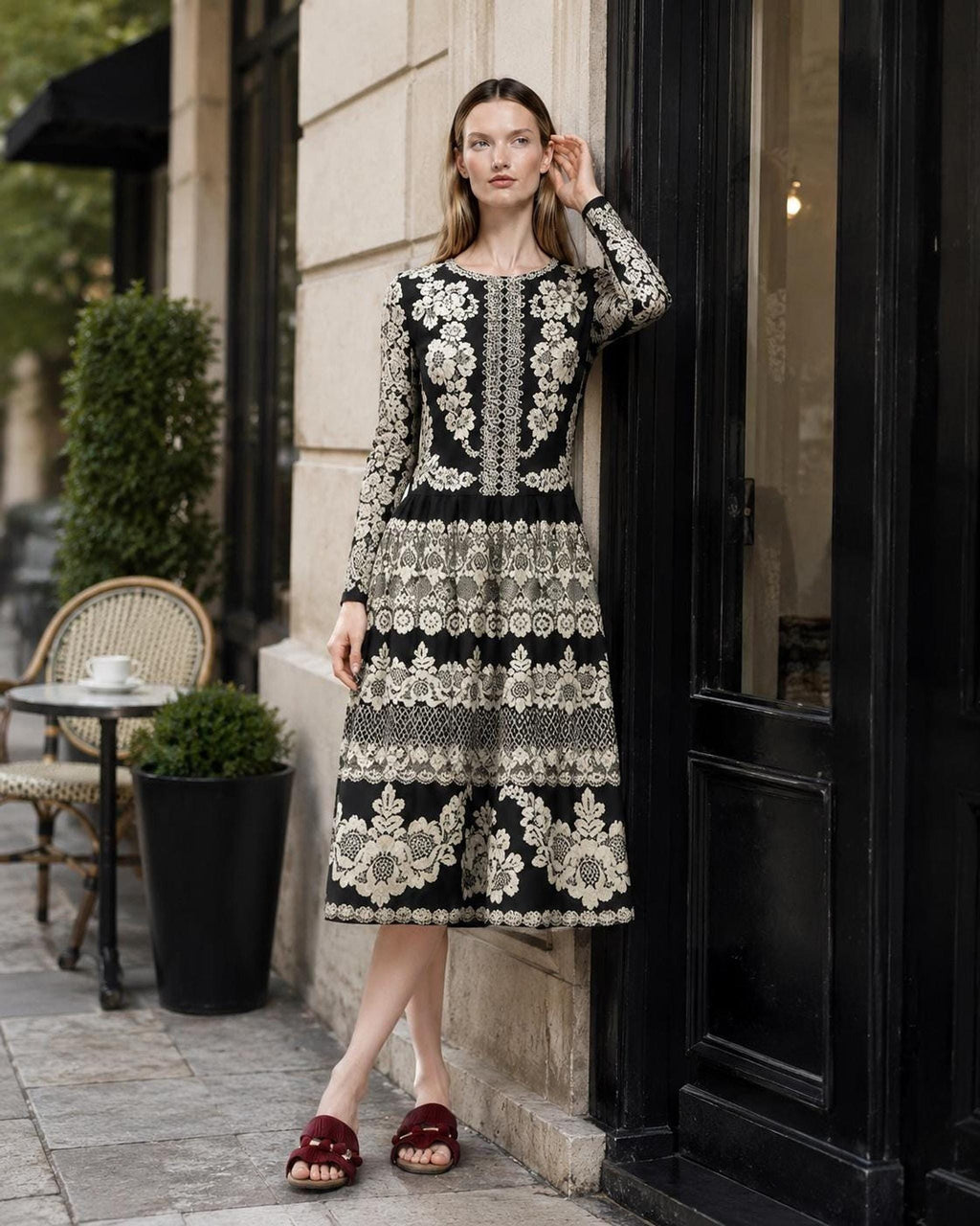Model leaning against a black doorframe on a city street, wearing the long-sleeved black and ivory patterned dress.