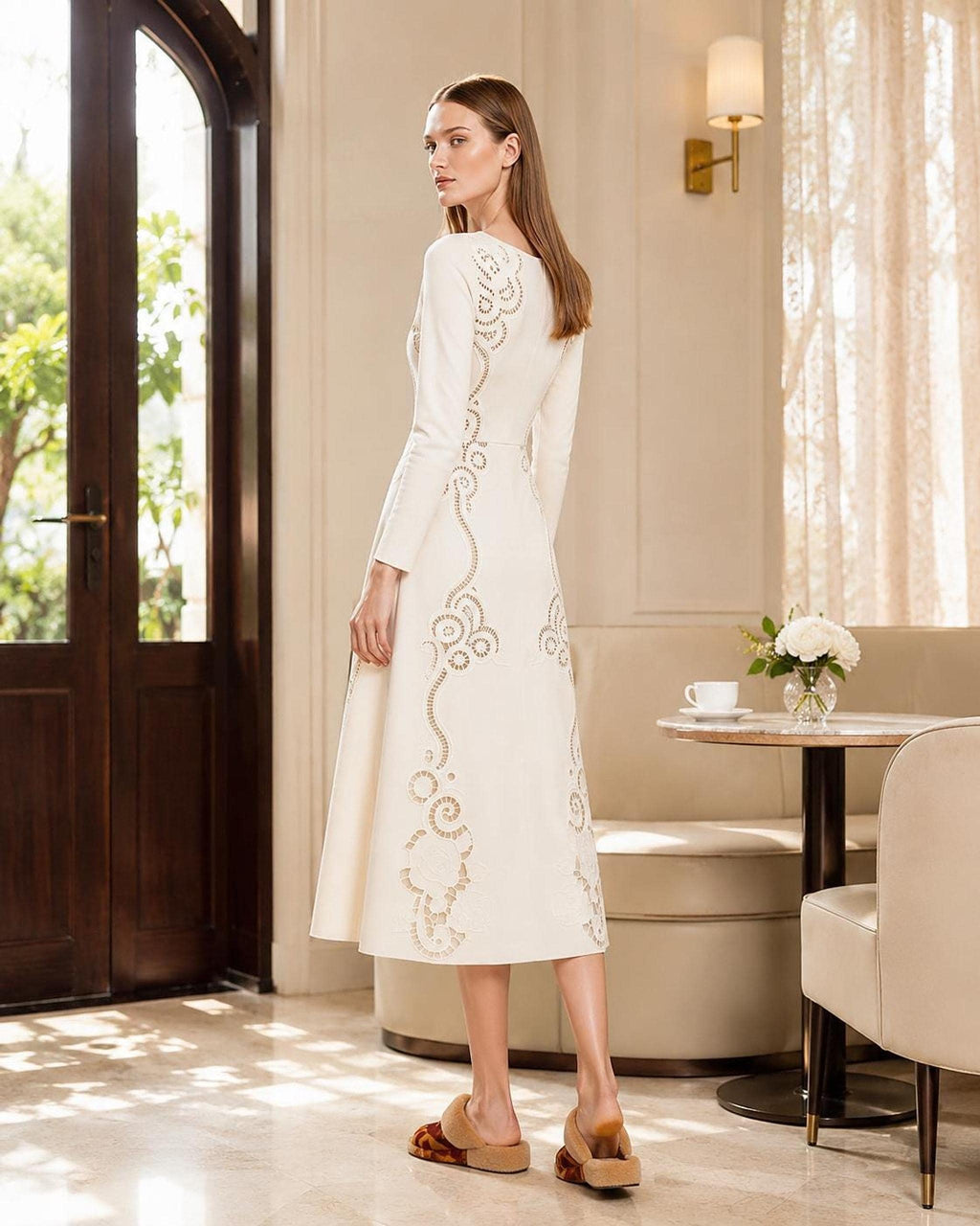 The same model turned sideways, showcasing the back view of the long-sleeved ivory midi dress with trailing eyelet patterns.