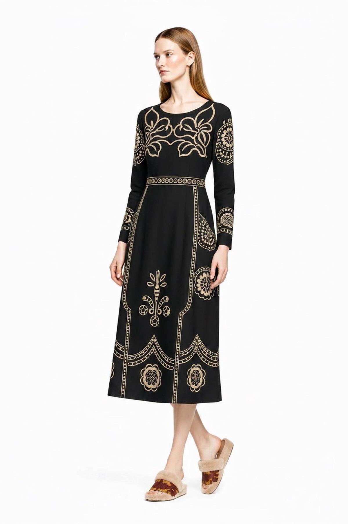 A model poses at a slight angle wearing the black midi dress with beige floral patterns and fluffy slip-on sandals.
