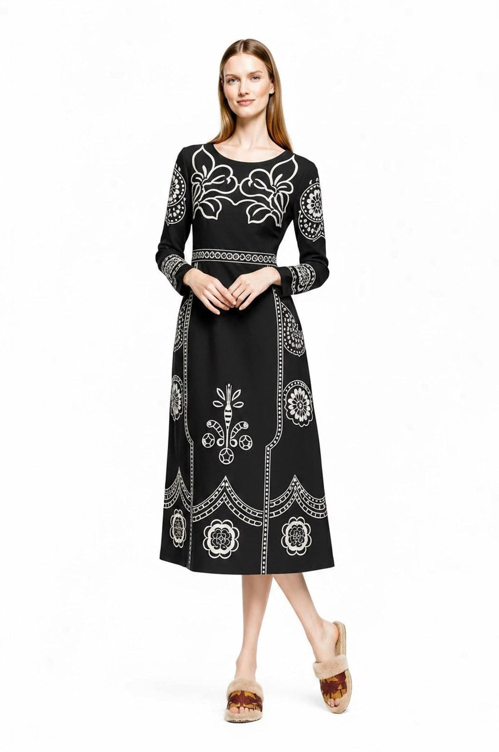 A model poses with hands clasped in front, wearing the black midi dress with white print and fluffy sandals.