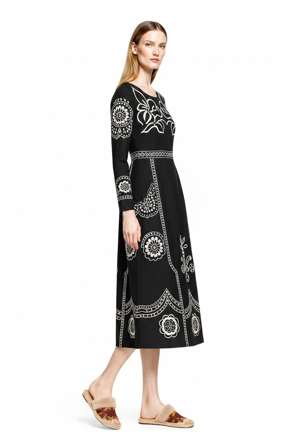 A profile view of a model wearing the black and white folk floral print midi dress against a plain white background.