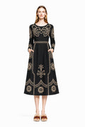 A model stands facing forward wearing a black midi dress with beige folk floral print and long sleeves against a plain white background.