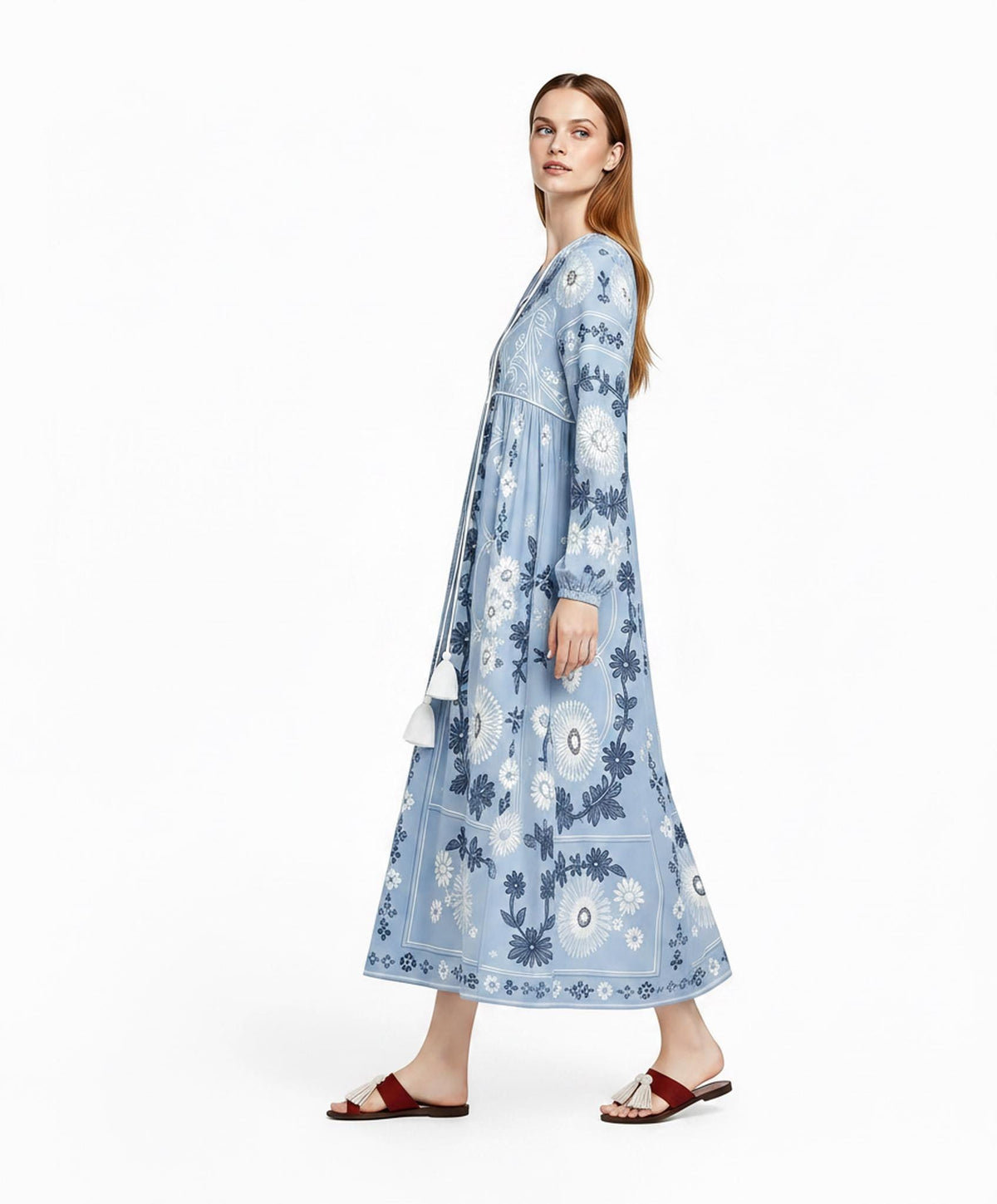 May include: A light blue long-sleeved maxi dress featuring a white and dark blue floral pattern, a V-neckline with a drawstring closure ending in two white tassels, and gathered cuffs. The dress is paired with dark red slide sandals with tassels.